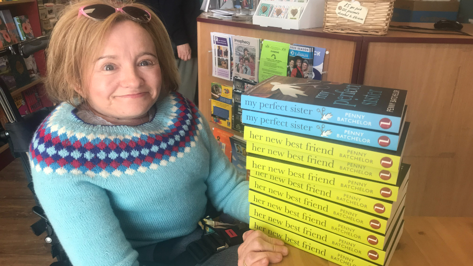 The image shows Penny Batchelor with a stack of her books titled 'My Perfect Sister' and 'Her new best friend'.